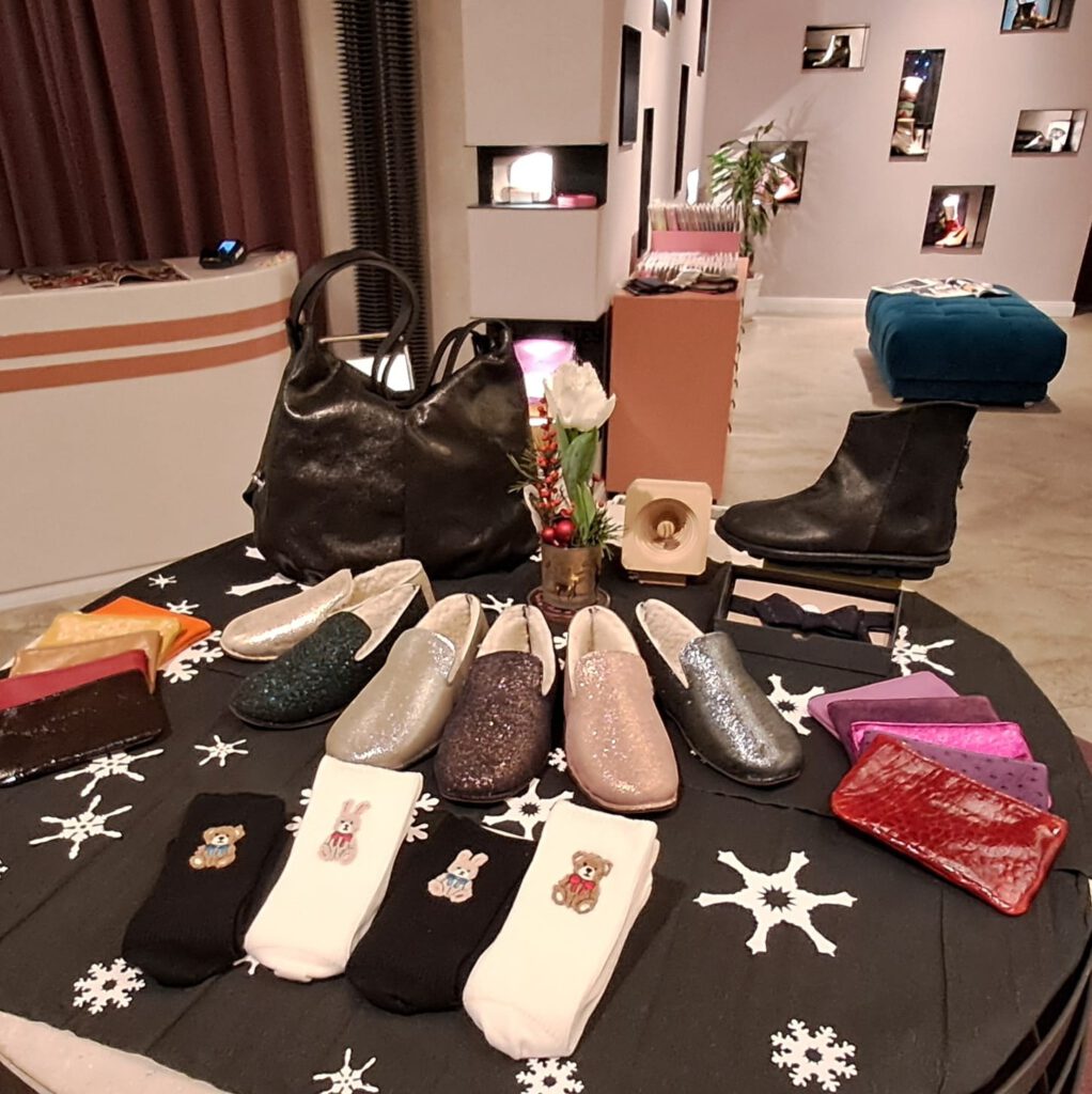 Flauschige, glitzernde Hausschuhe mit echter Wolle, daneben schlichte einfarbige Geldbeutel, davor Tabio Haussocken mit niedlichen gestickten Hasen- oder Bärenmotiven mit Schleifen um den Hals und dahinter ein passendes Set in glitzerndem Schwarz, bestehend aus Stiefeletten und einer Umhängetasche.